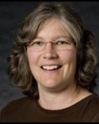 Close up photo of a person with medium-length curly brown/grey hair smiling with glasses