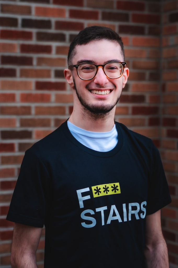 Latino man smiling wearing brown glasses and a black F*** STAIRS T-SHIRT. 